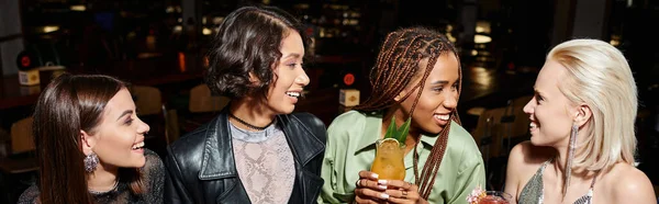 Novias multirraciales felices y de moda con copas de cóctel hablando en bar, pancarta horizontal - foto de stock
