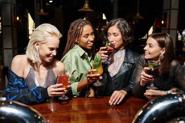 Young asian woman drinking cocktail near cheerful multiethnic girlfriends in bar, party time — Stock Photo