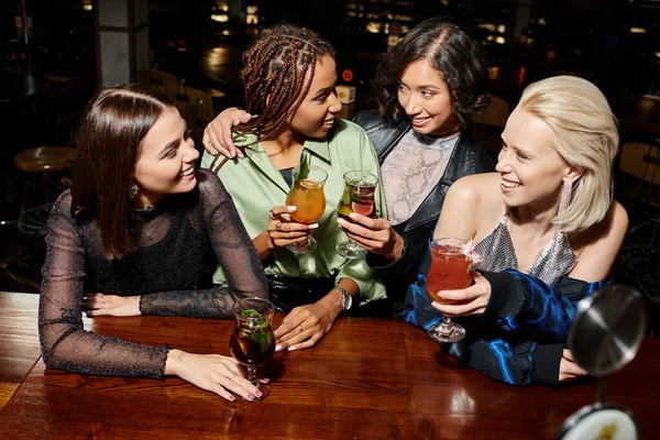 Trendy multicultural female friends toasting with cocktails during leisure in bar, glamorous party — Stock Photo