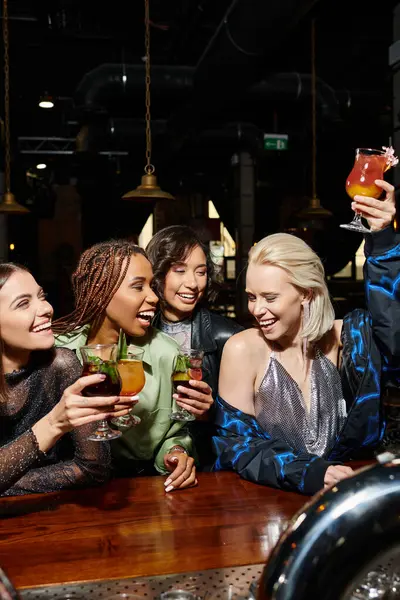 Excited blonde woman toasting with cocktail during hen party with multiethnic girlfriends in bar — Stock Photo