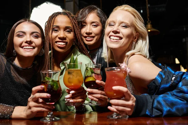 Young and glamorous women with delicious cocktails smiling at camera, entertainment in bar — Stock Photo