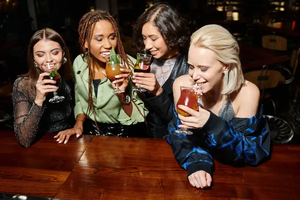 Fashionistas multirraciais felizes bebendo deliciosos coquetéis durante a festa no bar, atmosfera festiva — Fotografia de Stock