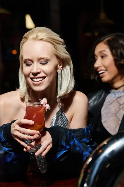 Ravi femme blonde avec verre de délicieux cocktail près de petite amie multiculturelle dans le bar — Photo de stock