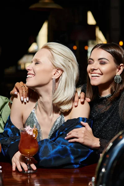Heureux et glamour jeunes femmes souriant avec les yeux fermés près du verre de délicieux cocktail dans le bar — Photo de stock