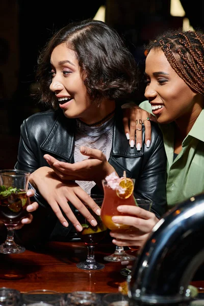 Stylish african american and asian girlfriends smiling near delicious cocktails in bar, party time — Stock Photo