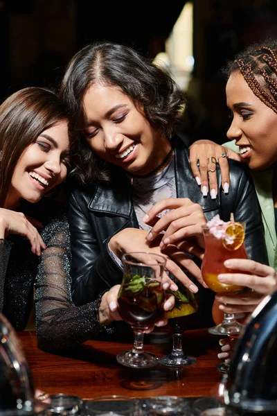 Happy multiracial fashionistas with cocktail glasses smiling with closed eyes in bar, hen party — Stock Photo