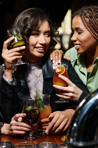 Alluring and stylish multiracial girlfriends smiling and holding delicious cocktails in bar — Stock Photo