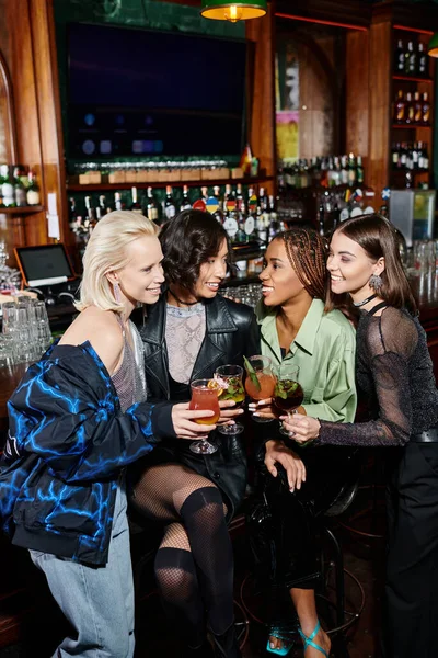 Модные и счастливые многонациональные девушки в коктейльных очках проводят время в современном баре — стоковое фото