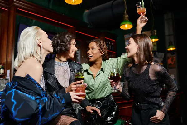Excited african american woman toasting with cocktail near elegant multiethnic girlfriends in bar — Stock Photo