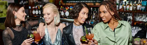 Счастливые и модные многонациональные подруги, держащие коктейли и разговаривающие в баре, горизонтальный баннер — стоковое фото