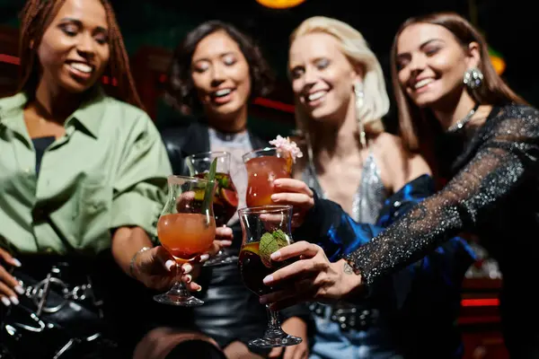 Souriant et élégant multiethnique copines clinking cocktails dans le bar sur fond flou — Photo de stock