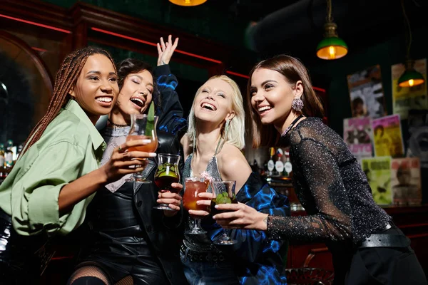 Fashionistas multiétnicos alegres com deliciosos coquetéis se divertindo no bar, atmosfera vibrante — Fotografia de Stock