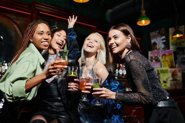 Cheerful multiethnic fashionistas with delicious cocktails having fun in bar, vibrant atmosphere — Stock Photo