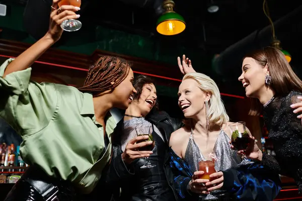 Cheerful and stylish multicultural girlfriends with cocktails glasses dancing in bar, party time — Stock Photo