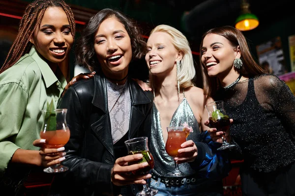 Giovani e glamour fidanzate multietniche con bicchieri da cocktail sorridenti nel bar, addio al nubilato — Foto stock