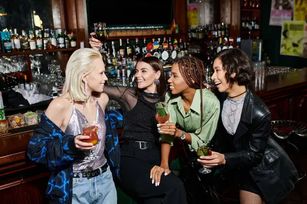 Despreocupadas amigas multiétnicas que celebran cócteles y hablan en un bar moderno, tiempo de fiesta - foto de stock