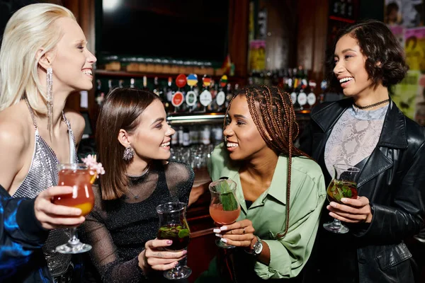 Jeunes et élégantes amies multiraciales avec des cocktails parlant au bar, temps de fête dynamique — Photo de stock