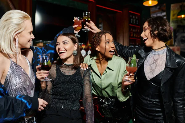 Беззаботные многорасовые девушки звонят в коктейльные бокалы в современном баре, счастье и досуг — стоковое фото