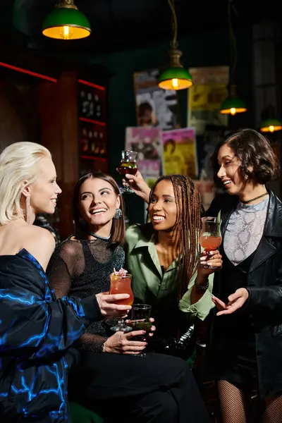 Joyful asian woman toasting with cocktail near trendy multiethnic girlfriends in bar, leisure time — Stock Photo