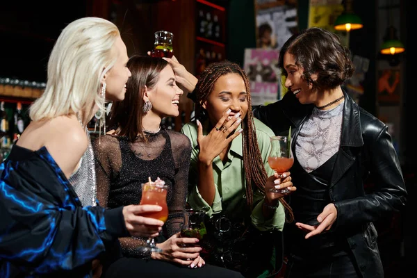 Веселая африканская американка смеется рядом с многонациональными подругами в коктейльных бокалах в баре — стоковое фото