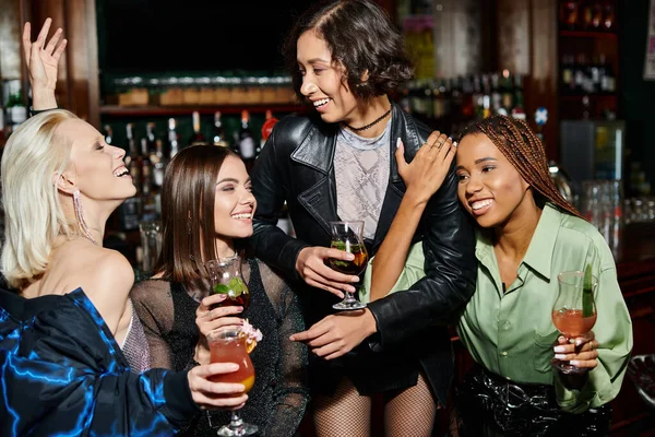 Souriant asiatique femme debout avec cocktail verre près joyeuse multiculturelle copines dans bar — Photo de stock
