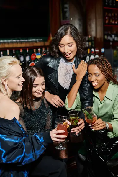 Stylish and happy multicultural female friends clinking cocktail glasses in bar, modern lifestyle — Stock Photo