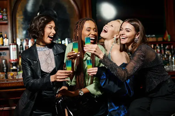 Novias multirraciales alegres y de moda con gafas de chupito riendo en el bar moderno, despedida de soltera - foto de stock