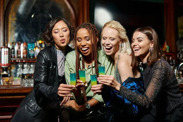 Joyful and stylish multiracial girlfriends clinking shot glasses during festive party in bar — Stock Photo