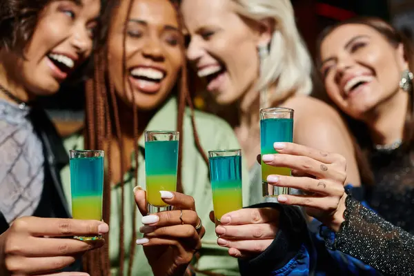Selective focus of shot glasses near cheerful multiethnic girlfriends on blurred background — Stock Photo