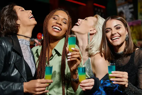 Happy multicultural girlfriends with shot glasses smiling with closed eyes during party in bar — Stock Photo