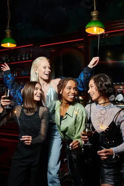 Namoradas multiétnicas alegres com coquetéis e faíscas festivas se divertindo no bar, tempo de festa — Fotografia de Stock