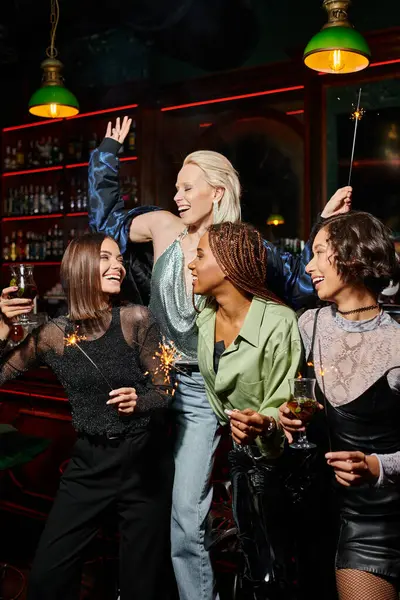 Переполненные радостью многонациональные девушки с коктейлями и сверкающими искрами, веселящиеся в баре, время вечеринок — стоковое фото