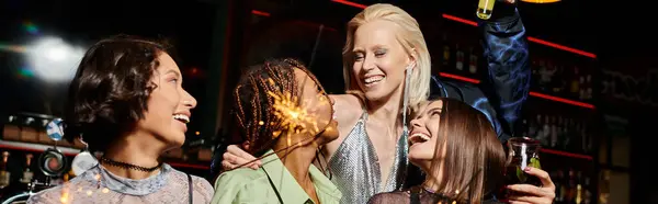 Cheerful multiethnic girlfriends with cocktails and shiny sparklers having party in bar, banner — Stock Photo