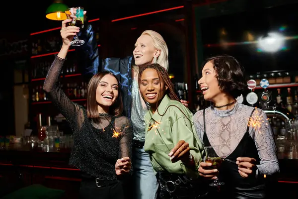 Excitadas novias multiculturales brindando con cócteles y celebrando brillantes chispas en el bar - foto de stock
