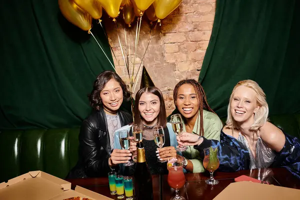 Excited multiethnic girlfriends toasting with champagne near golden balloons in bar, birthday party — Stock Photo