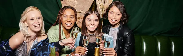 Молодые и стильные многонациональные девушки с бокалами для шампанского, улыбающиеся перед камерой в баре, баннер — стоковое фото