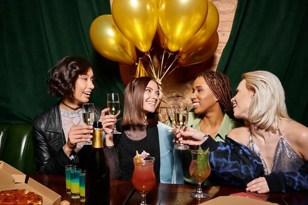 Joyful multiethnic women with champagne celebrating birthday of girlfriend in party hat in bar — Stock Photo