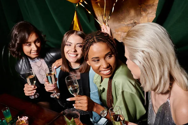 Overjoyed and elegant multiracial women holding champagne glasses during birthday party in bar — Stock Photo