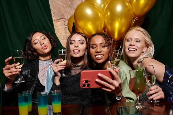 Стильные многонациональные девушки с шампанским, делающие селфи на смартфоне в баре, день рождения — стоковое фото