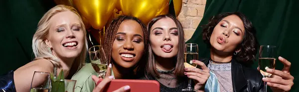 Cheerful multiethnic women with champagne grimacing and taking selfie on mobile phone in bar, banner — Stock Photo
