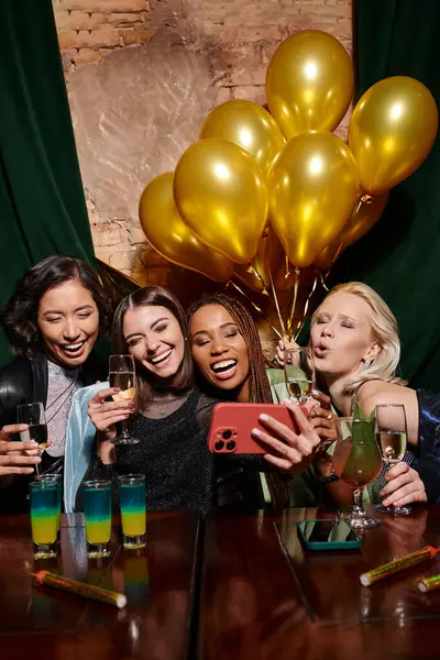 Carefree multiracial women taking selfie near cocktails and golden balloons in bar, birthday party — Stock Photo