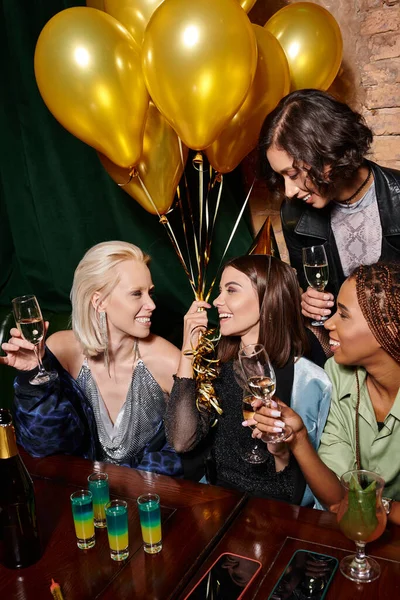 Happy woman in party hat with golden balloons celebrating birthday with multiracial girlfriends — Stock Photo