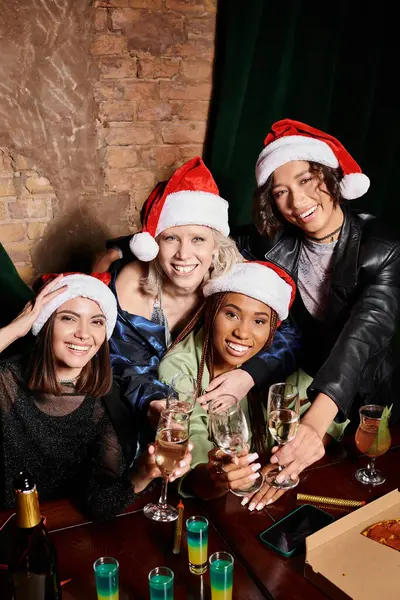 Joyeuses femmes multiculturelles cliquetis verres à champagne et regarder la caméra dans le bar, fête de Noël — Photo de stock