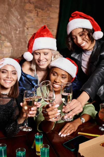 Despreocupados novias multiétnicas tintineo copas de champán mientras se celebra la Navidad en el bar - foto de stock