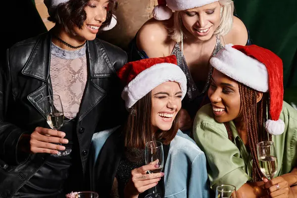 Novias despreocupadas multiculturales en sombreros de Navidad celebrando el Año Nuevo con champán en el bar - foto de stock