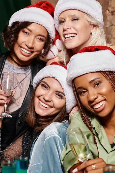 Портрет взволнованных многорасовых женщин с шампанским, смотрящих в камеру в баре, Рождественская вечеринка — стоковое фото