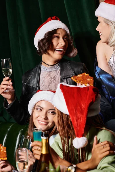 Alegres y elegantes novias multiétnicas celebrando la Navidad con bebidas alcohólicas y pizza en el bar - foto de stock