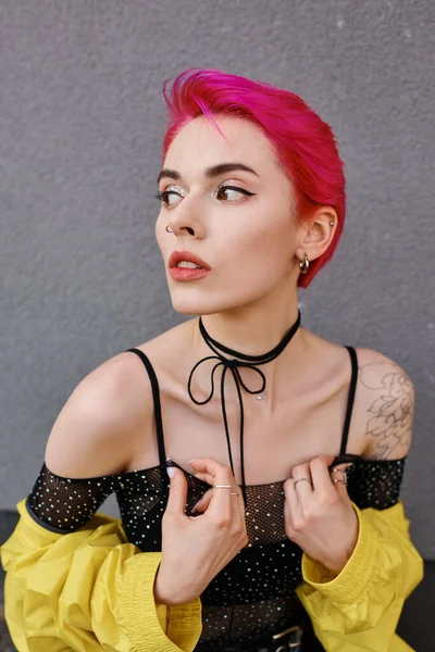 Portrait of alluring tattooed woman in yellow jacket posing on street and looking away, fashion — Stock Photo
