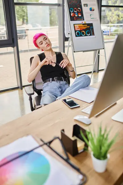 Junge Arbeiterin mit rosa Haaren sitzt mit Stift und schaut auf Computer, Geschäftskonzept — Stockfoto