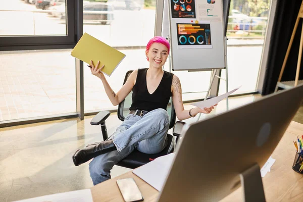 Allegra giovane operaia sorridente alla macchina fotografica del computer che tiene i suoi appunti, concetto di business — Foto stock